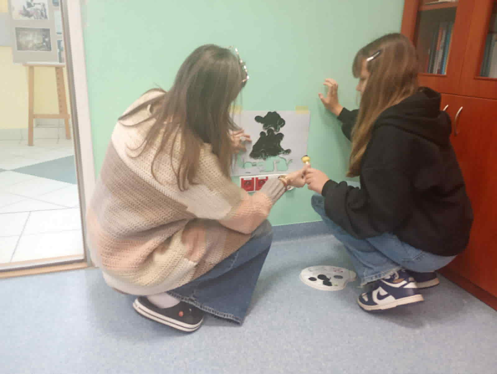 uczeń i nauczyciel malują coś na ścianie