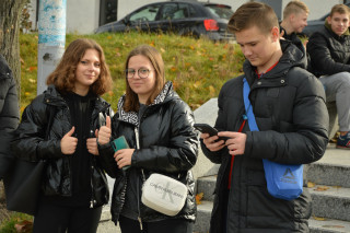 Dwie uczennice na Placu Wolności pozują do zdjęcia, uczeń patrzy na telefon.