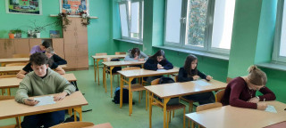 W klasie uczniowie siedzą w ławkach i piszą tekst dyktanda.