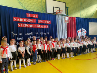 Przedszkolaki stoją przed dekoracją na sali gimnastycznej z okazji Narodowego Święta Niepodległości.