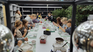 Uczniowie siedzą przy stole i malują własne bombki.