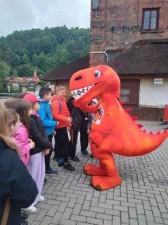 Uczniowie witają się z dinozaurem-maskotką Bałtowskiego Kompleksu Turystycznego