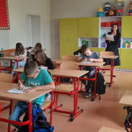 Uczniowie klas V i VI w sali piszą dyktando czytane przez nauczycielkę.