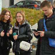 Dwie uczennice na Placu Wolności pozują do zdjęcia, uczeń patrzy na telefon.