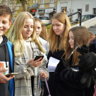 Uczniowie z kl. 7b na Placu Wolności wykonują zadania na telefonie podczas gry miejskiej.