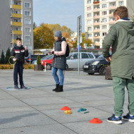 Nauczycielka i dwóch uczniów na placu przed Wojewódzkim Domem Kultury przygotowują się do wykonania zadania sportowego w czasie gry miejskiej.