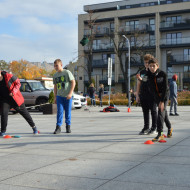 Czterech uczniów na placu przed Wojewódzkim Domem Kultury wykonują zadanie sportowe w czasie gry miejskiej.