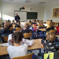 Uczniowie w sali lekcyjnej słuchają prowadzącego zajęcia policjanta.