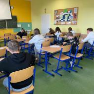 W klasie uczniowie siedzą w ławkach i piszą tekst dyktanda.