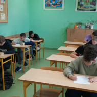 W klasie uczniowie siedzą w ławkach i piszą tekst dyktanda.