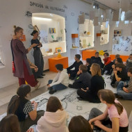 Uczniowie siedzą na podłodze i słuchają opowieści autorki wystawy.