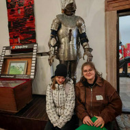 Uczennice siedzą przed repliką zbroi rycerskiej