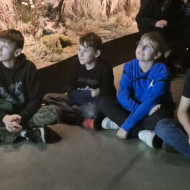 Uczniowie siedzą na podłodze i słuchają prelekcji.