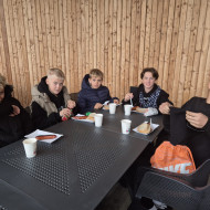 Uczniowie siedzą przy stole i jedzą kiełbaski z grilla.