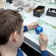 Uczeń ozdabia bombkę brokatem podczas warsztatów