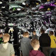 Grupa osób przechodzi przez tunel imitujący wnętrze szklanej bombki.