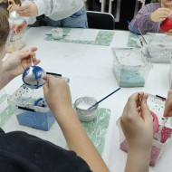 Uczeń ozdabia bombkę brokatem podczas warsztatów.