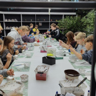 Uczniowie siedzą przy stole i malują własne bombki.