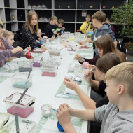 Uczniowie siedzą przy stole i malują własne bombki.