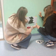 dwie osoby kucają i malują coś na ścianie