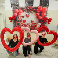 Uczennice z czerwonymi balonami w kształcie serc na tle ścianki walentynkowej..