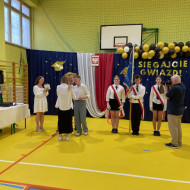 Sala gimnastyczna w szkole, Pani Prezydent wraz z Panem Dyrektorem wręczają nagrodę absolwenta roku