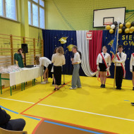 Sala gimnastyczna w szkole, Pani Prezydent wraz z Panem Dyrektorem wręczają nagrodę absolwenta roku