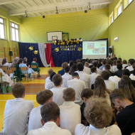Sala gimnastyczna w szkole, w tle prezentacja wspominająca historię klas 8