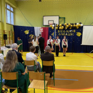 Sala gimnastyczna w szkole, rodzice odbierają nagrody w imieniu ucznia