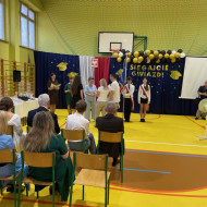 Sala gimnastyczna w szkole, rodzice odbierają nagrodę wraz z uczennicą