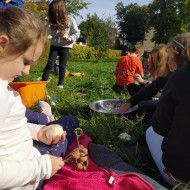 Grupka uczniów na trawniku wykonuje drzewka szczęścia.