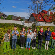 Grupka uczniów, na trawniku przed szkołą, prezentuje wykonane drzewka szczęścia