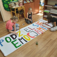Uczniowie malują farbami napis podziel się emocjami.