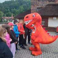 Uczniowie witają się z dinozaurem-maskotką Bałtowskiego Kompleksu Turystycznego