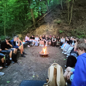 Uczniowie siedzą przy ognisku i słuchają opowieści pani przewodnik.