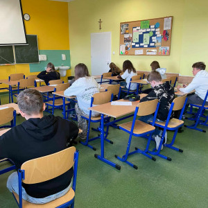 W klasie uczniowie siedzą w ławkach i piszą tekst dyktanda.