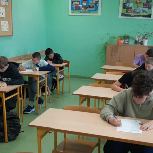 W klasie uczniowie siedzą w ławkach i piszą tekst dyktanda.