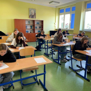 W klasie uczniowie siedzą w ławkach i piszą tekst dyktanda.