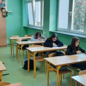 W klasie uczniowie siedzą w ławkach i piszą tekst dyktanda.