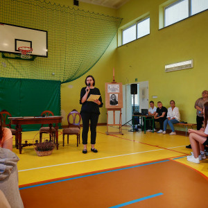 Nauczycielka stoi i przemawia do uczestników imprezy w sali gimnastycznej.