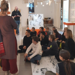 Uczniowie siedzą na podłodze i słuchają opowieści o Edmundzie Niziurskim.