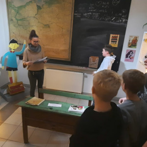 Uczeń stopi przed czarną tablicą i zapisuje zadanie w grze na podstawie powieści "Przygody Marka Piegusa"