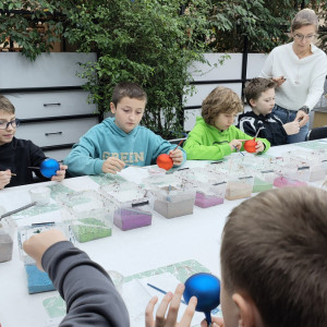 Dzieci dekorują bombki różnymi kolorami farb.