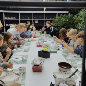 Uczniowie siedzą przy stole i malują własne bombki.