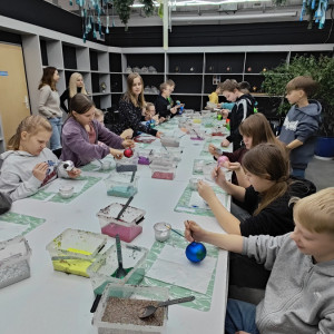 Uczniowie siedzą przy stole i malują własne bombki.