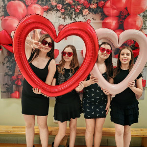 Uczennice trzymają balony w kształcie serc i pozują przed walentynkową ścianką.