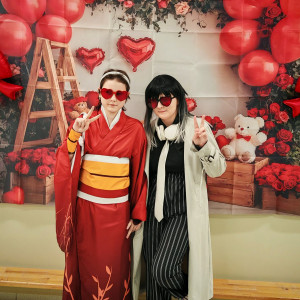 Dwie uczennice w oryginalnych strojach na tle walentynkowej ścianki. 