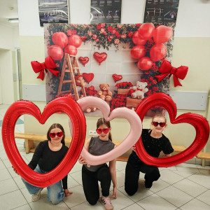Uczennice z czerwonymi balonami w kształcie serc na tle ścianki walentynkowej..