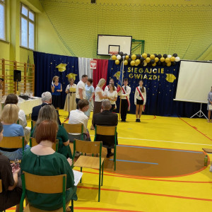 Sala gimnastyczna w szkole, uczennica odbiera dyplom wraz z rodzicami