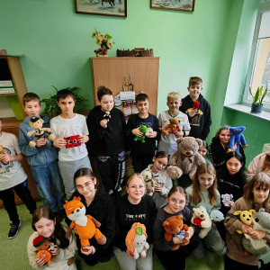 Uczniowie z klasy 5 przebywają w rogu sali lekcyjnej i prezentują swoje misie i maskotki.